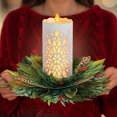 Decorative candle with greenery held by a person wearing a red sweater.