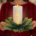 Decorative candle with greenery held by a person wearing a red sweater.
