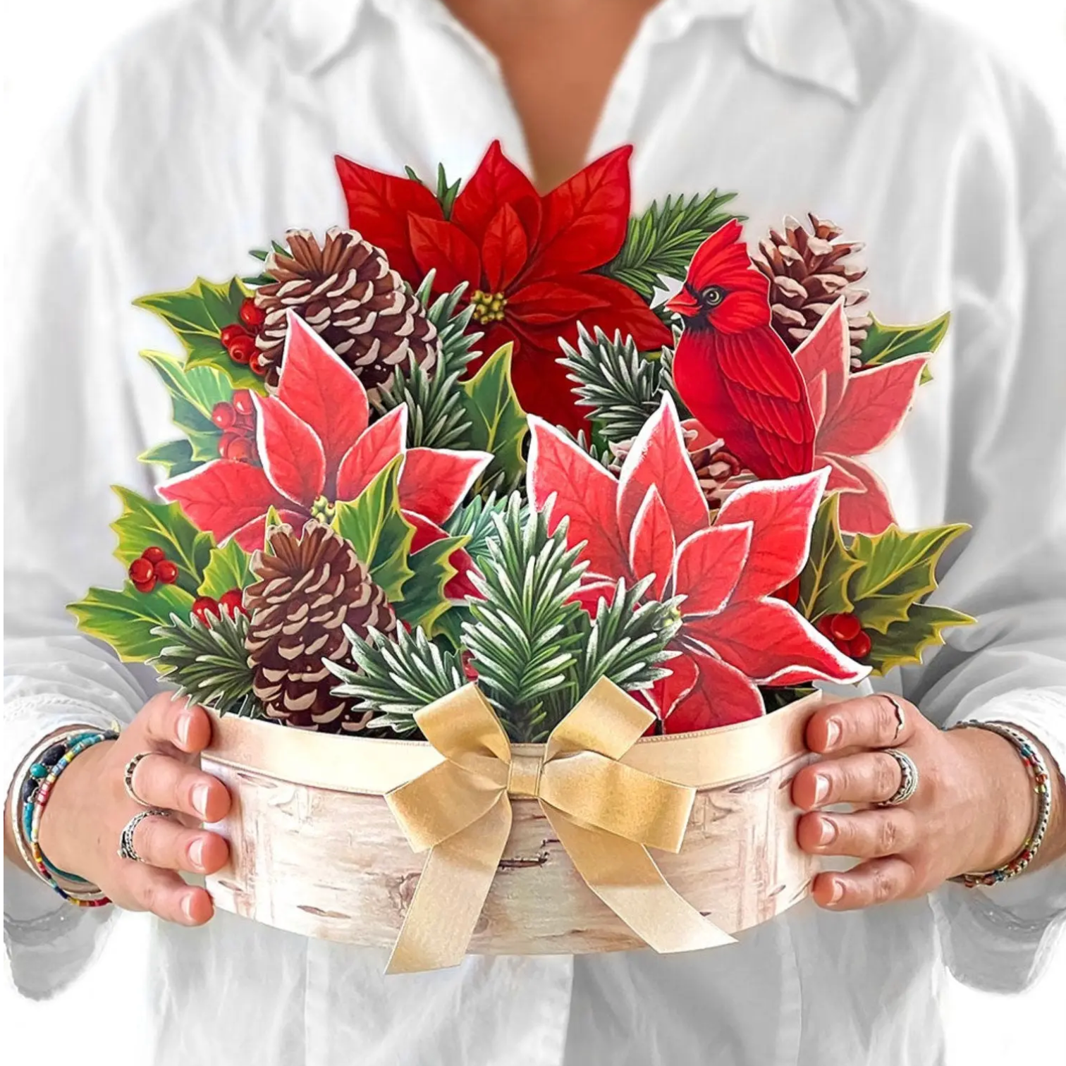 Person holding a decorative Christmas flower arrangement with poinsettias, cardinal, and pinecones.