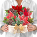 Person holding a decorative Christmas flower arrangement with poinsettias, cardinal, and pinecones.