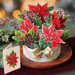 Decorative Christmas arrangement with poinsettias, pinecones, and a card on a wooden surface.